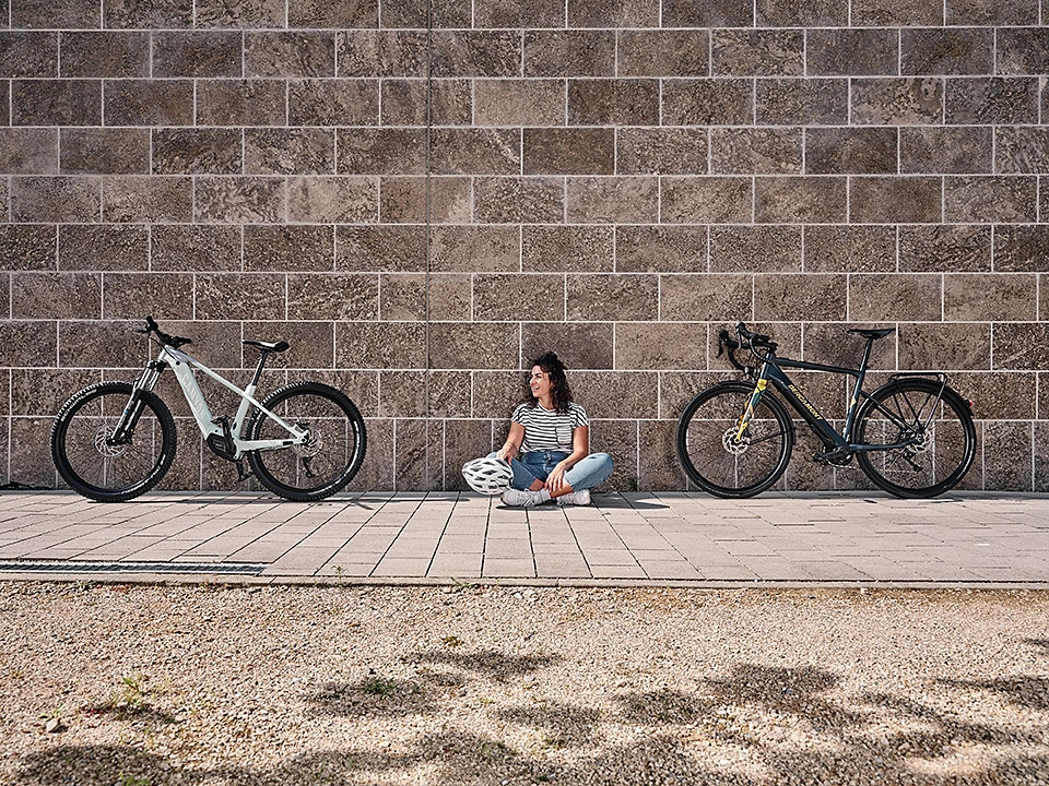 Eine Frau sitzt vor einer Mauer zwischen zwei Fahrrädern Eine Frau sitzt vor einer Mauer zwischen zwei Fahrrädern