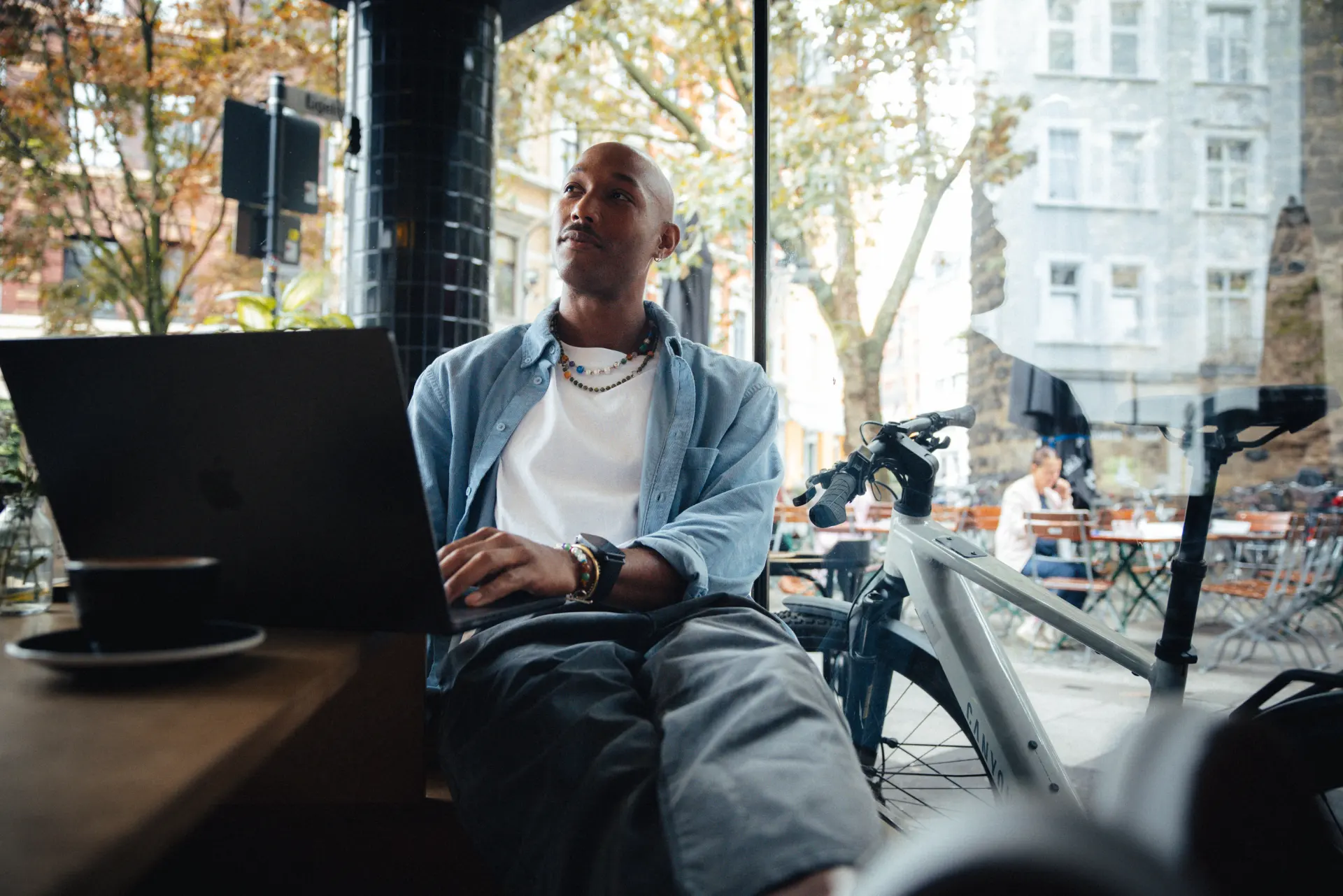 Mann mit Laptop im Cafe schaut JobRad Angebote an, draussen am Fenster lehnt sein schickes Canyon E-Bike